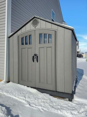 snow covered structure featuring an outbuilding and a storage shed