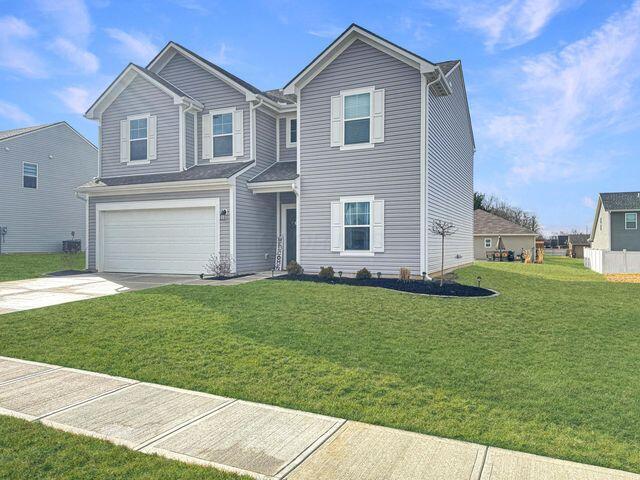 traditional home featuring a garage, concrete driveway, and a front lawn