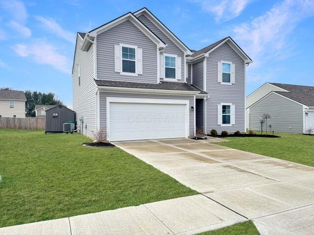 traditional home with concrete driveway, an attached garage, fence, central air condition unit, and a front lawn