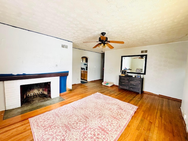 unfurnished living room featuring a textured ceiling, a brick fireplace, hardwood / wood-style flooring, and ceiling fan