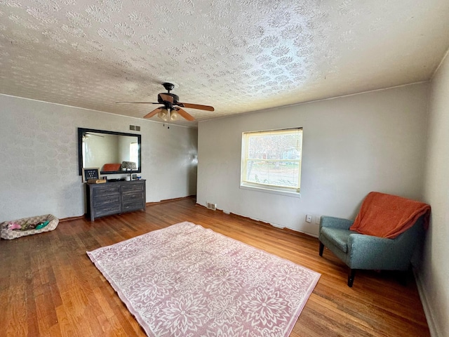 living area featuring hardwood / wood-style flooring, a textured ceiling, and ceiling fan