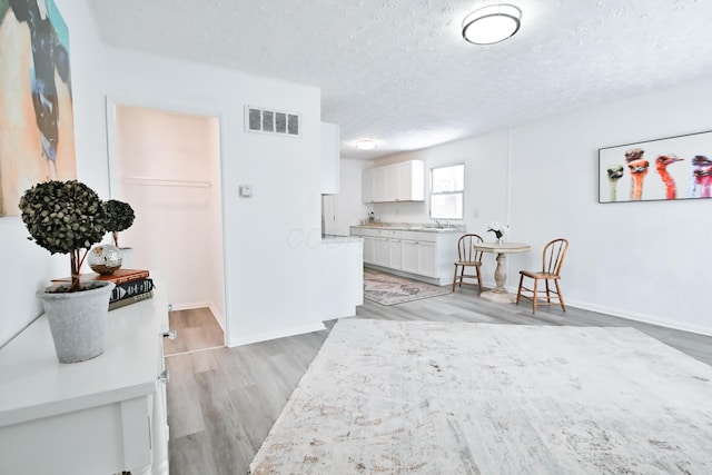 kitchen with sink, white cabinets, a textured ceiling, and light hardwood / wood-style floors