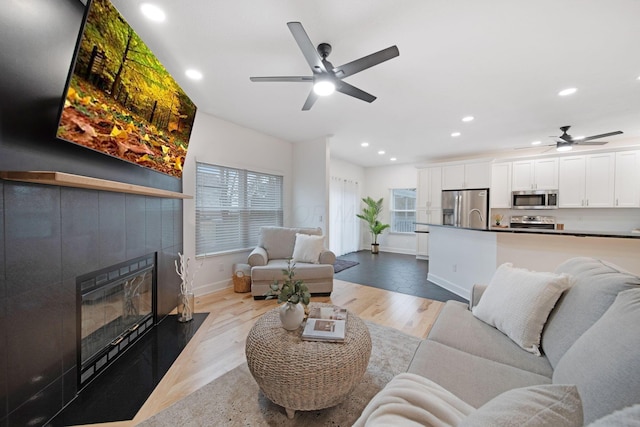 living room with ceiling fan, a wealth of natural light, a tiled fireplace, and light wood-type flooring