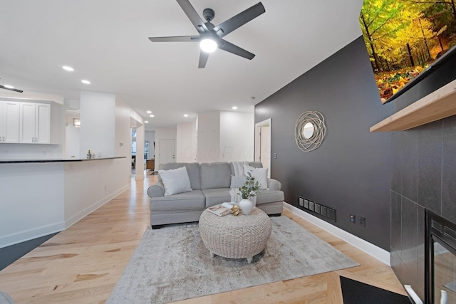 living room featuring ceiling fan, a tiled fireplace, and light wood-type flooring