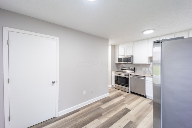 kitchen with a textured ceiling, light wood-type flooring, backsplash, white cabinetry, and appliances with stainless steel finishes