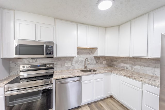 kitchen featuring sink, white cabinets, a textured ceiling, light wood-type flooring, and appliances with stainless steel finishes