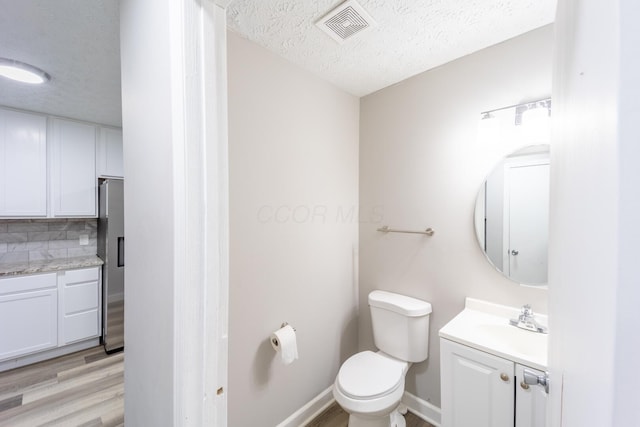 bathroom with tasteful backsplash, a textured ceiling, vanity, and toilet