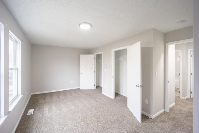 unfurnished bedroom with a textured ceiling, multiple windows, and light carpet