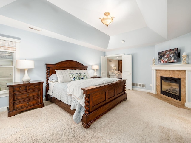 bedroom featuring a tile fireplace, light colored carpet, and a tray ceiling