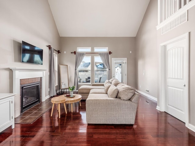 living room featuring high vaulted ceiling, dark hardwood / wood-style floors, and a tiled fireplace