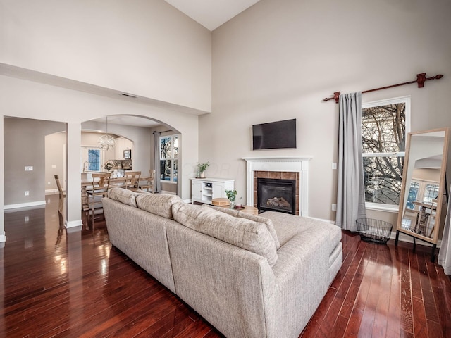 living room with a fireplace, dark wood-type flooring, an inviting chandelier, and a towering ceiling