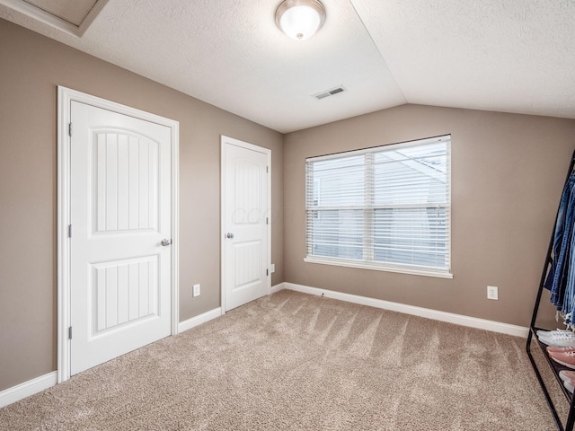 unfurnished bedroom featuring vaulted ceiling, carpet, and a textured ceiling