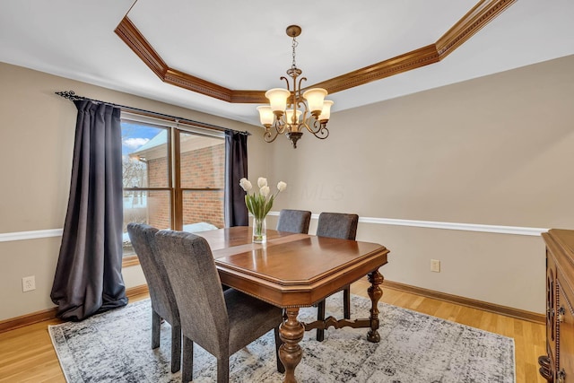 dining area with light wood-type flooring, a chandelier, and a raised ceiling