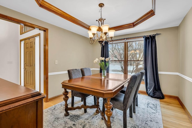 dining area with a raised ceiling, light wood-type flooring, a notable chandelier, and ornamental molding