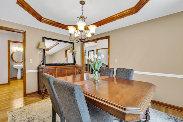 dining room with light wood-type flooring, an inviting chandelier, crown molding, and a raised ceiling