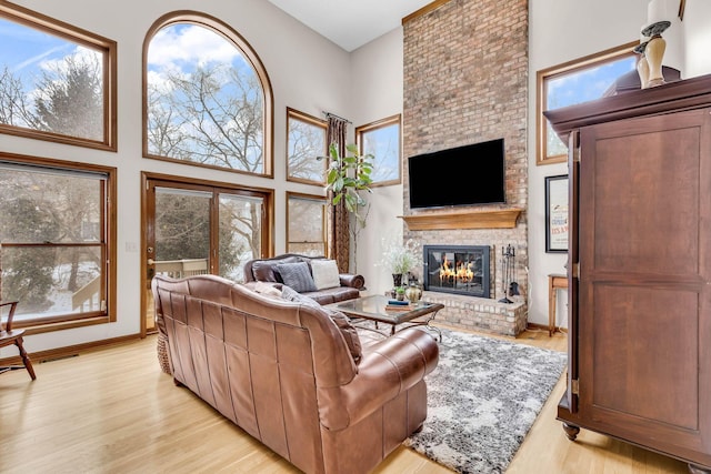 living room featuring a high ceiling, light wood-type flooring, plenty of natural light, and a fireplace