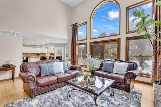 living room with a high ceiling, a notable chandelier, and light wood-type flooring