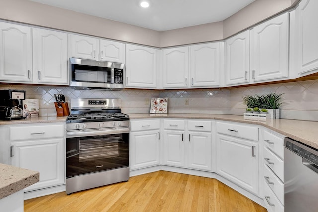 kitchen featuring light wood-type flooring, appliances with stainless steel finishes, white cabinetry, and tasteful backsplash