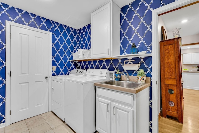 clothes washing area with washer and clothes dryer, sink, light tile patterned floors, and cabinets