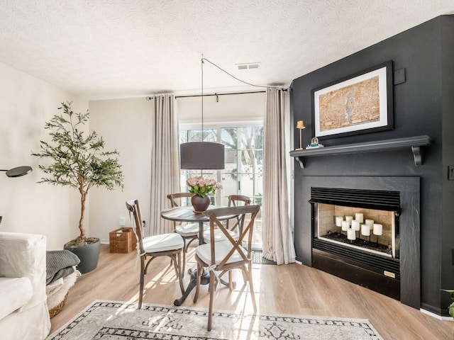 dining room featuring hardwood / wood-style flooring, a large fireplace, and a textured ceiling