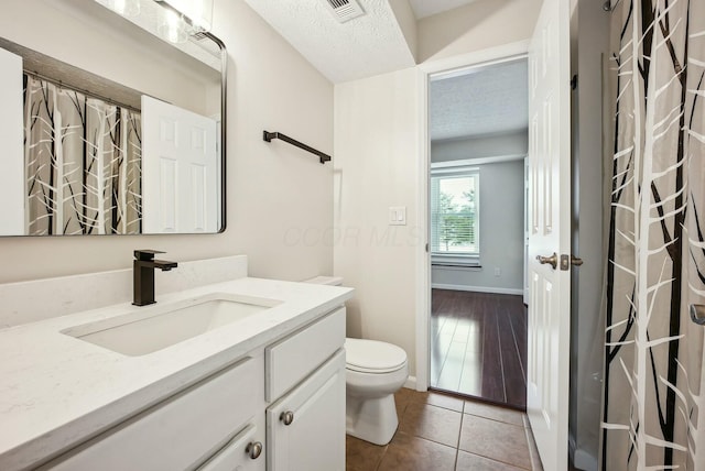 bathroom featuring a textured ceiling, toilet, tile patterned floors, and vanity