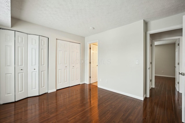 unfurnished bedroom featuring dark wood-type flooring, two closets, and a textured ceiling