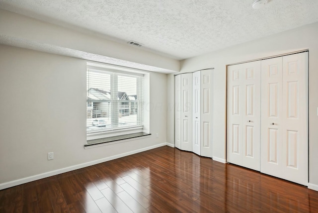 unfurnished bedroom featuring a textured ceiling, multiple closets, and dark hardwood / wood-style floors