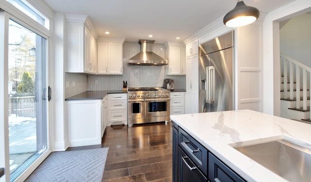 kitchen featuring tasteful backsplash, wall chimney range hood, white cabinetry, premium appliances, and dark wood-type flooring