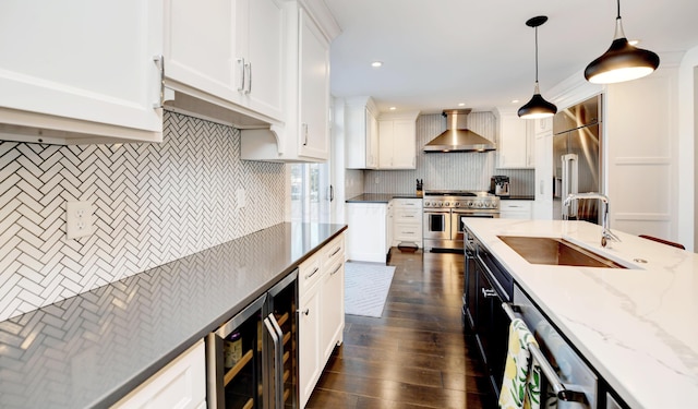 kitchen featuring decorative light fixtures, high end appliances, wall chimney exhaust hood, white cabinets, and sink