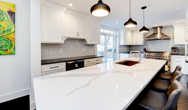 kitchen featuring white cabinetry, pendant lighting, range with two ovens, and wall chimney range hood