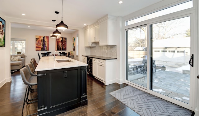 kitchen with a kitchen island with sink, white cabinets, hanging light fixtures, and sink