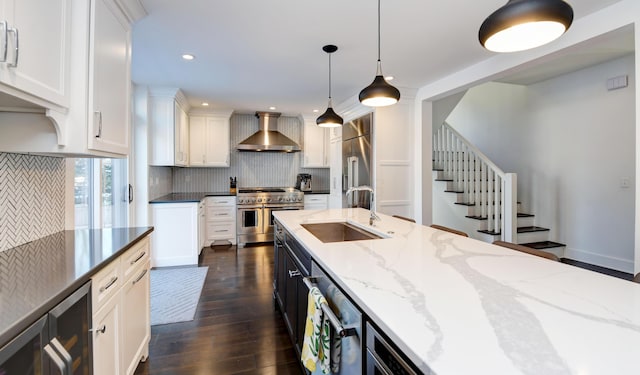 kitchen with wall chimney range hood, pendant lighting, sink, white cabinetry, and high quality appliances