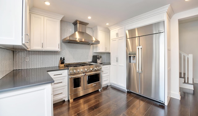 kitchen with backsplash, wall chimney range hood, white cabinets, and premium appliances