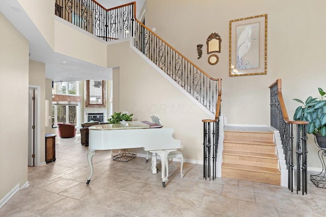 stairway featuring a glass covered fireplace, a high ceiling, and baseboards