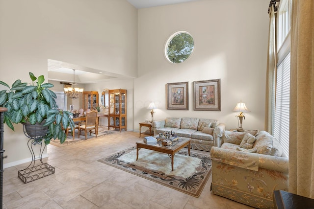 living area featuring a chandelier, a high ceiling, baseboards, and a healthy amount of sunlight