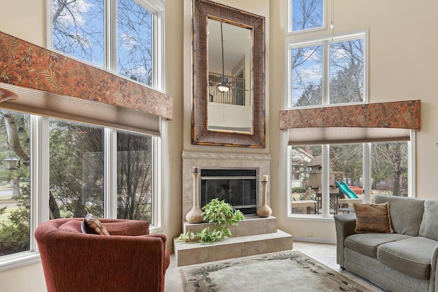 tiled living area featuring ceiling fan, a high ceiling, and a fireplace