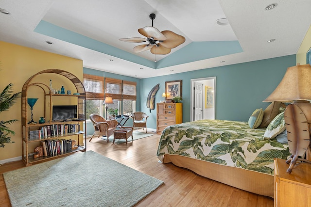 bedroom featuring light wood finished floors, baseboards, and a raised ceiling