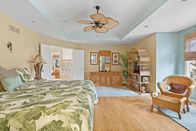 bedroom with light wood finished floors, visible vents, a raised ceiling, a ceiling fan, and lofted ceiling