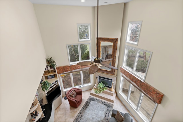 living area featuring light tile patterned floors, a towering ceiling, ceiling fan, a fireplace, and recessed lighting