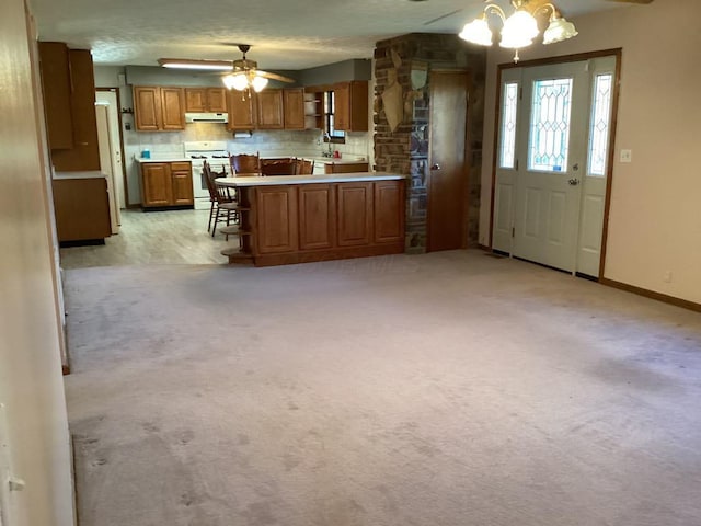 kitchen with white range with gas stovetop, a breakfast bar area, light colored carpet, hanging light fixtures, and sink