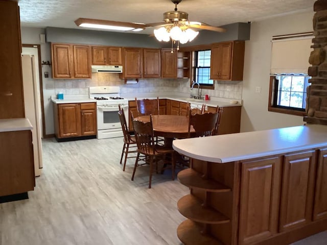 kitchen with white appliances, light hardwood / wood-style floors, sink, kitchen peninsula, and ceiling fan