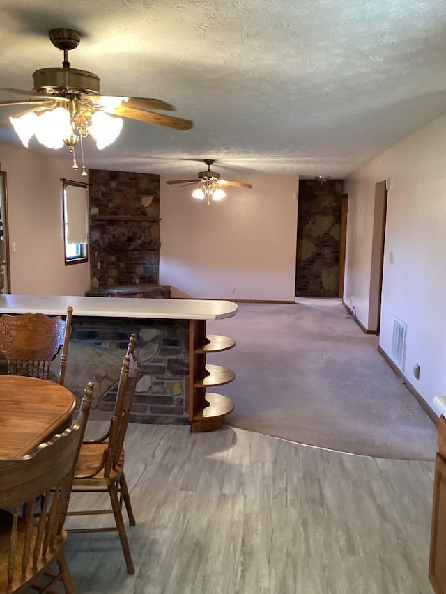 dining room featuring ceiling fan, light wood-type flooring, a fireplace, and a textured ceiling