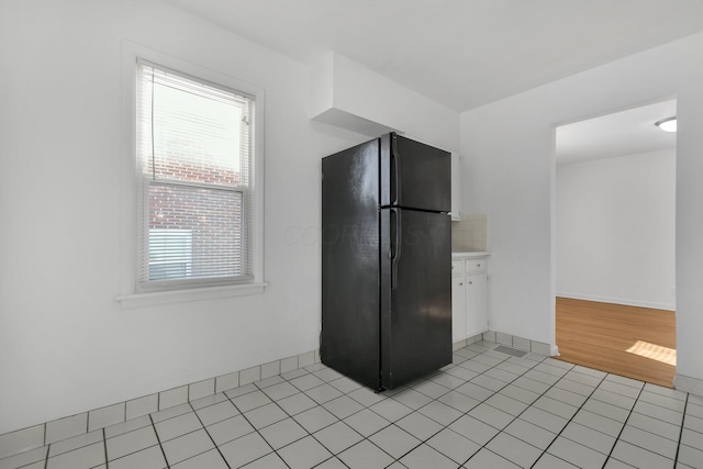 kitchen with decorative backsplash, black refrigerator, and light tile patterned floors