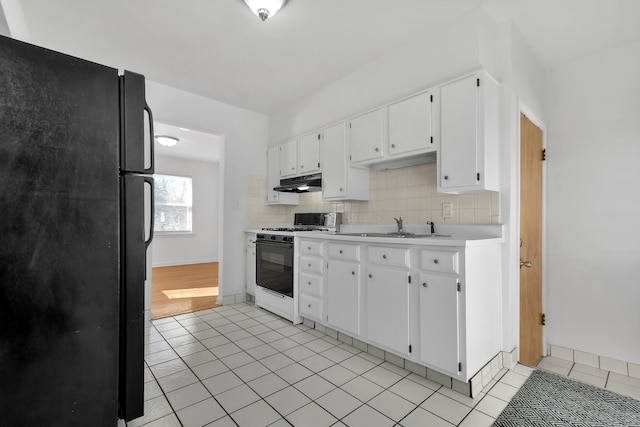 kitchen with white cabinets, gas range gas stove, tasteful backsplash, sink, and black fridge