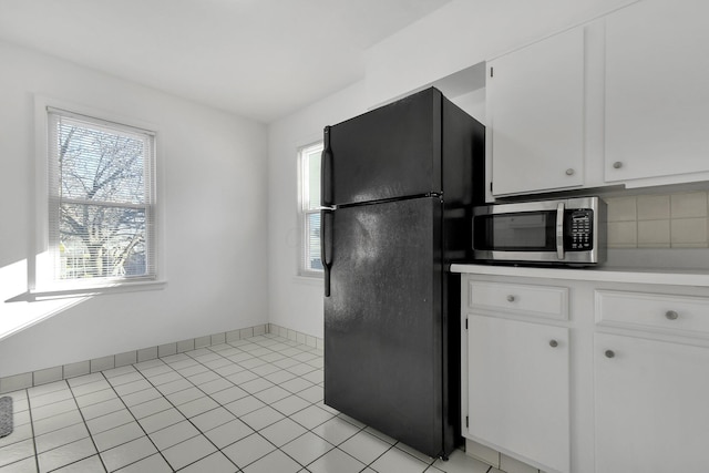 kitchen featuring decorative backsplash, black refrigerator, white cabinetry, and light tile patterned floors