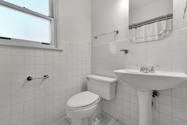 bathroom with toilet, tile patterned flooring, and tile walls