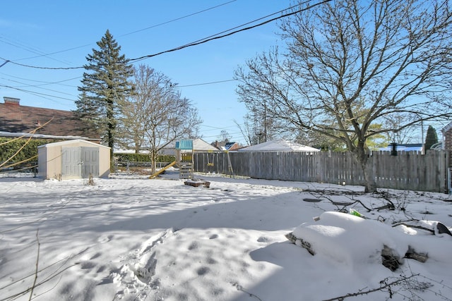 snowy yard with a playground and a storage shed