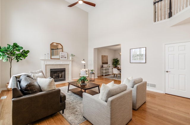 living room with high vaulted ceiling, ceiling fan, a fireplace, and light wood-type flooring