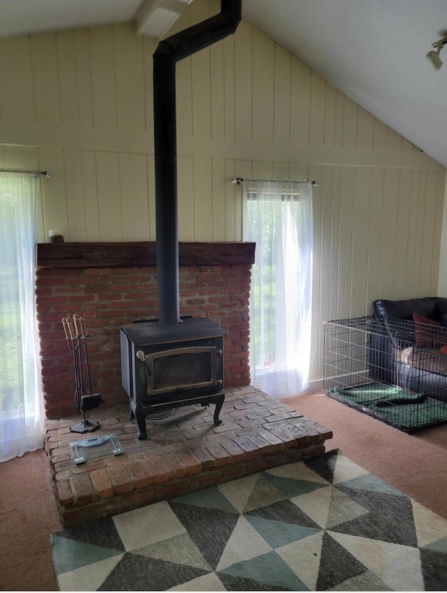 carpeted living room with lofted ceiling, wood walls, and a wood stove