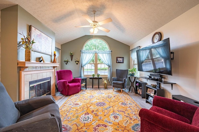 living room featuring a textured ceiling, vaulted ceiling, light hardwood / wood-style floors, a fireplace, and ceiling fan